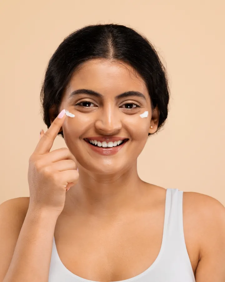 A woman smiling as she dabs moisturiser under her eye