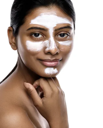A woman smiling with a white clay mask across her face