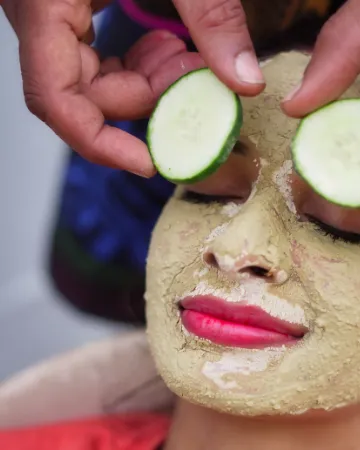 A woman with a clay face pack and cucumber slices over her eyes