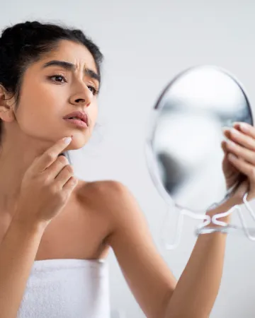A woman looking closely at her skin in a hand mirror